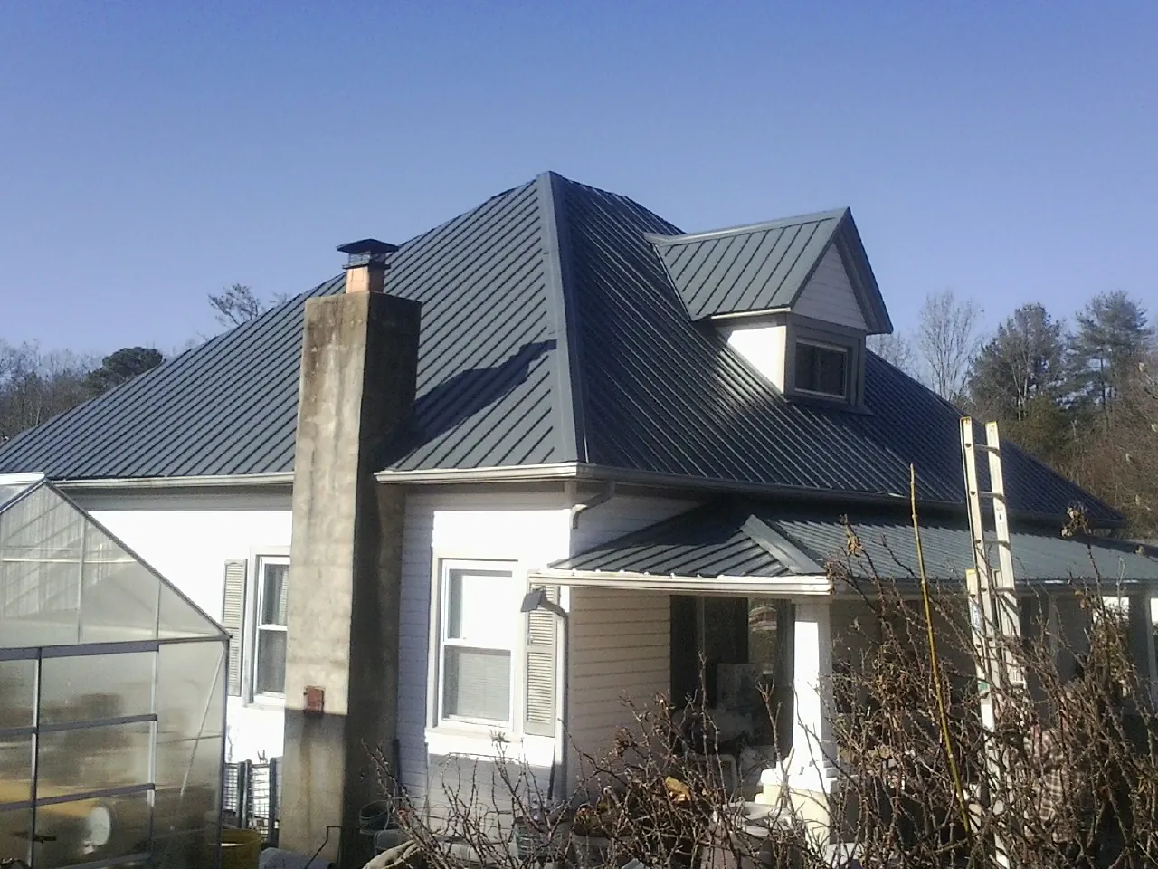 Dark blue standing seam metal roof on a white farmhouse with dormer — Slate & Tile Roof Repair by Roofing Brothers in Kaplan
