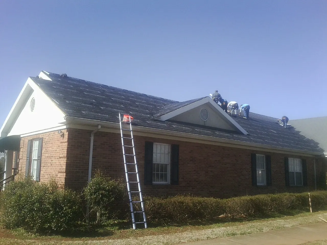 Crew tearing shingles off a brick ranch roof with a ladder set — Metal Roof Repair work by our crew in Kaplan