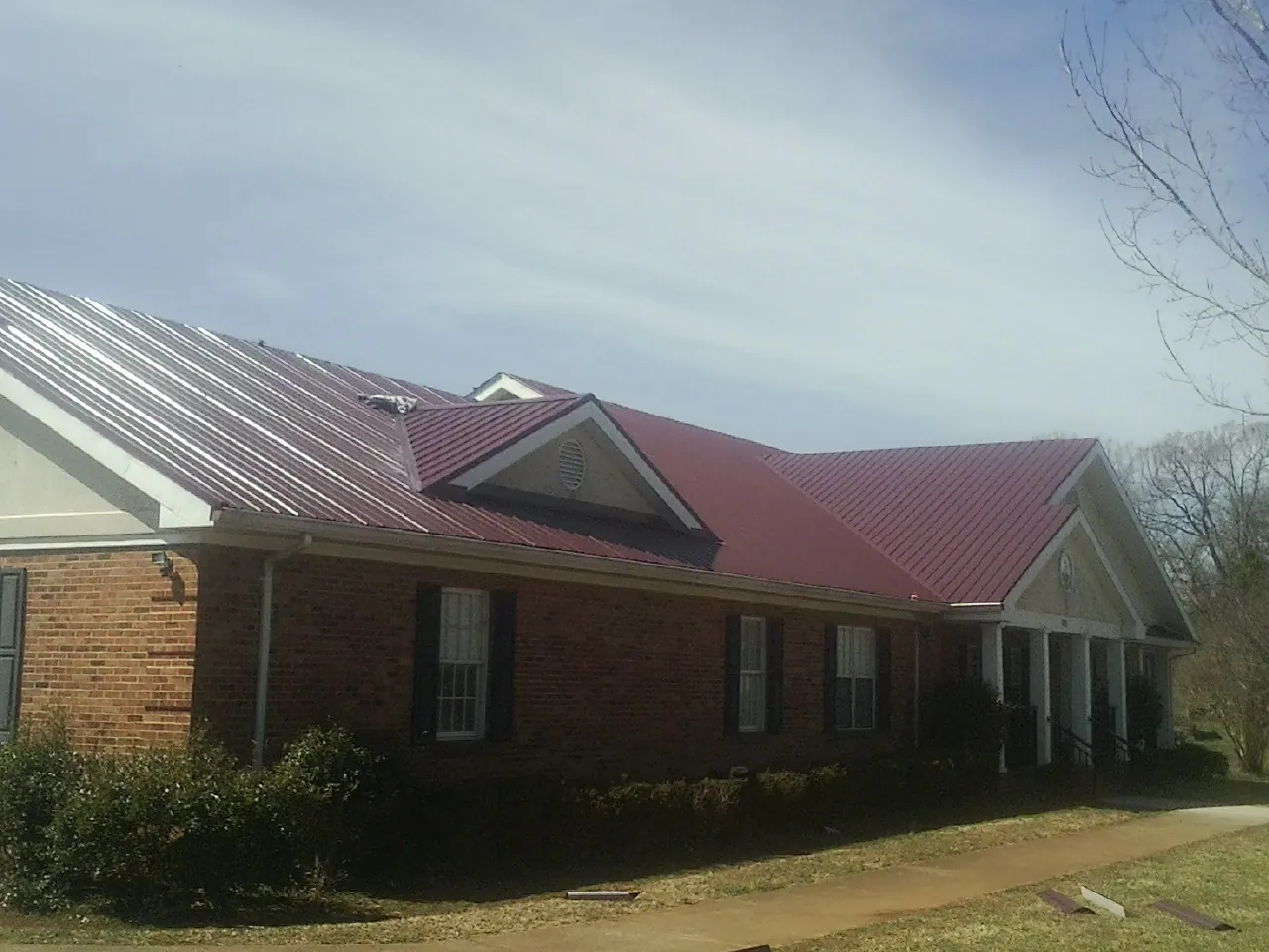 Red metal roof with gabled entries on a long brick building, from a Hail Damage Roof Repair job in Kaplan