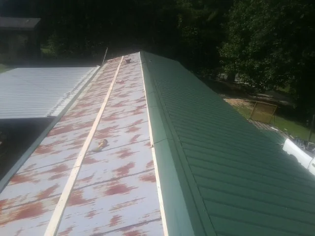 Old rusted panels beside newly installed green metal roofing — Wind Damage Roof Repair by Roofing Brothers in Kaplan