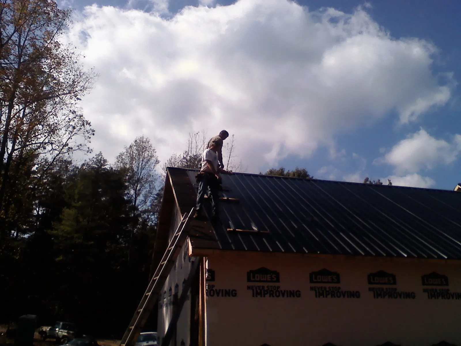 Roofer fastening dark metal panels high against a cloudy sky, from a Roof Inspection job in Kaplan